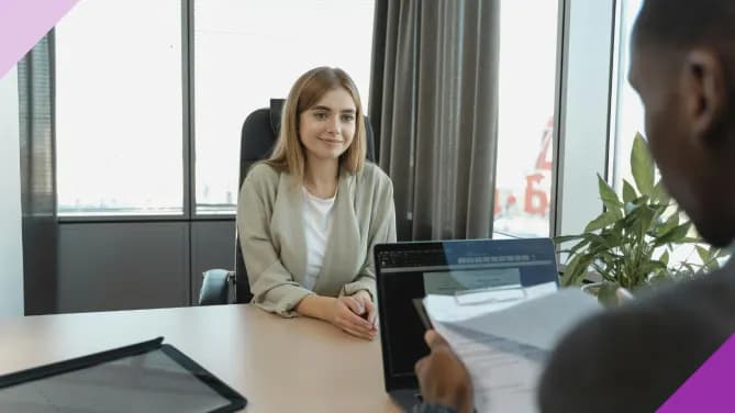 Woman wearing a blazer, sat across a table interviewing for a job, illustrating job interview etiquette regarding clothes