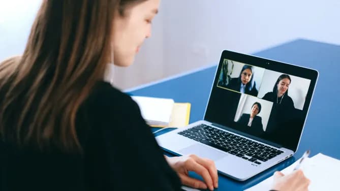 woman hunched over computer with earbuds in talking in a Zoom meeting with three other people
