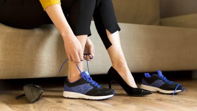 Woman changing high heels, office shoes after working day while sitting on the couch, ready to take a walk or run