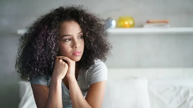 young woman sitting on her bed looking worried