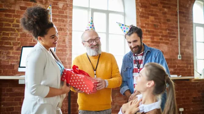 employees wearing party hats and giving gifts to a coworker