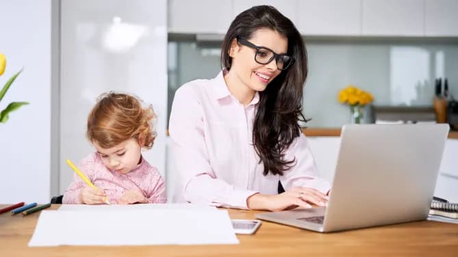 woman on her laptop while her toddler colors next to her