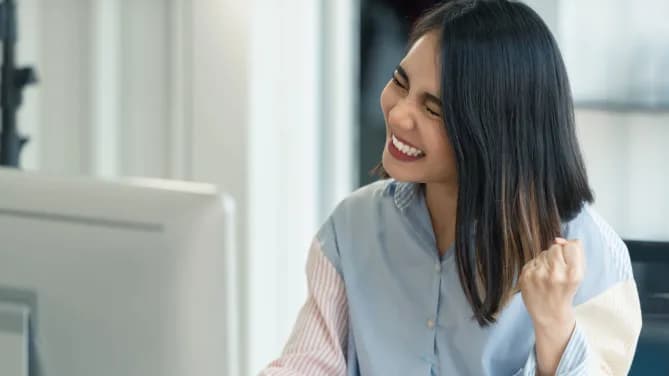 Women smiling with eyes closed and clenched fist in front of computer.