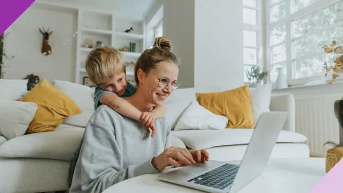 young mother working at computer with son wrapping her arms around her from behind