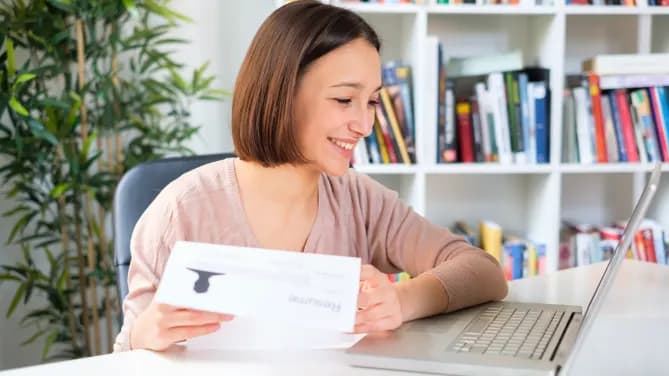 Woman smiling at laptop with resume in hand.