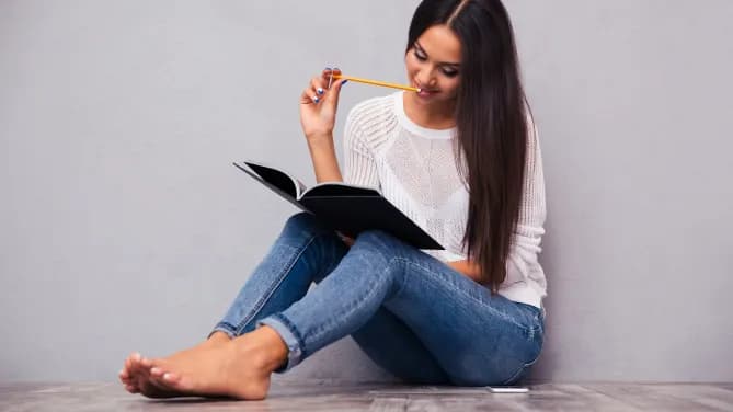 woman sitting with a notebook with a pencil in her mouth