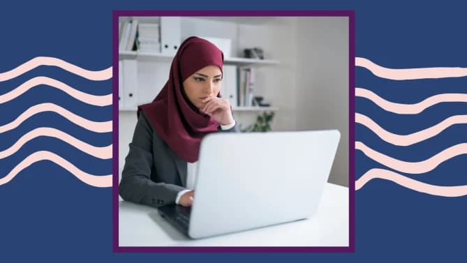 A woman wearing a dark red hijab working on a laptop.