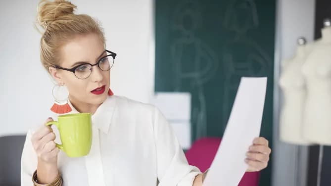 woman looking at a resume with a coffee in her hand