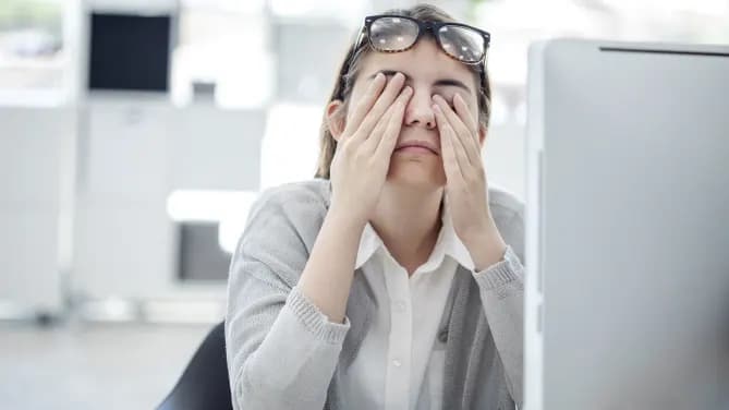tired woman rubbing her eyes at work