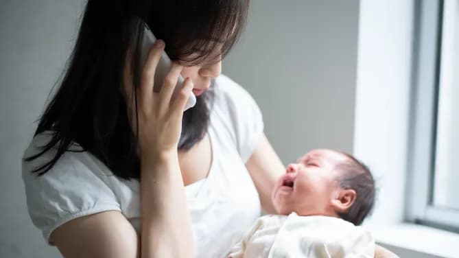 woman on the phone holding crying baby