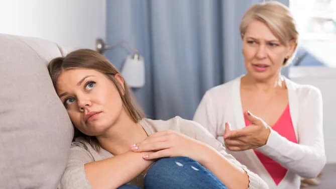 woman looking upset on the couch while her mother argues with her