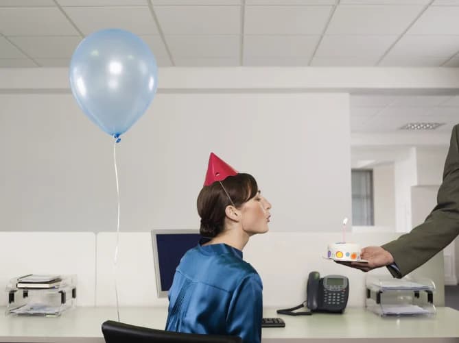 Woman blowing out birthday cake at work
