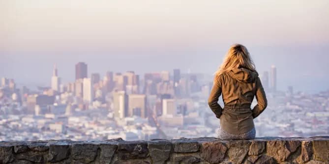 woman sitting on a stone wall looking out at a city