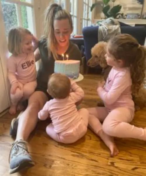 Laura and her kids sitting on the ground blowing out birthday cake candles